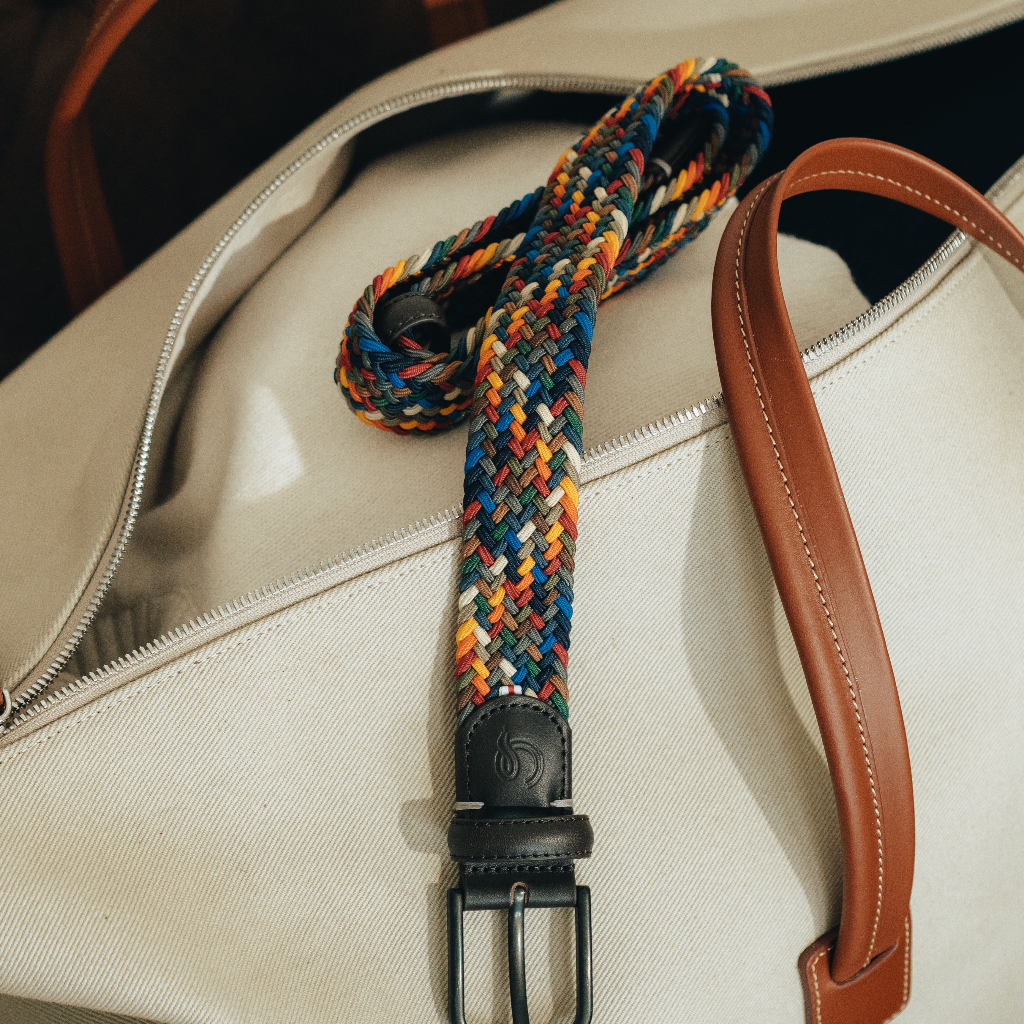Colorful braided belt with a black buckle on a white bag.