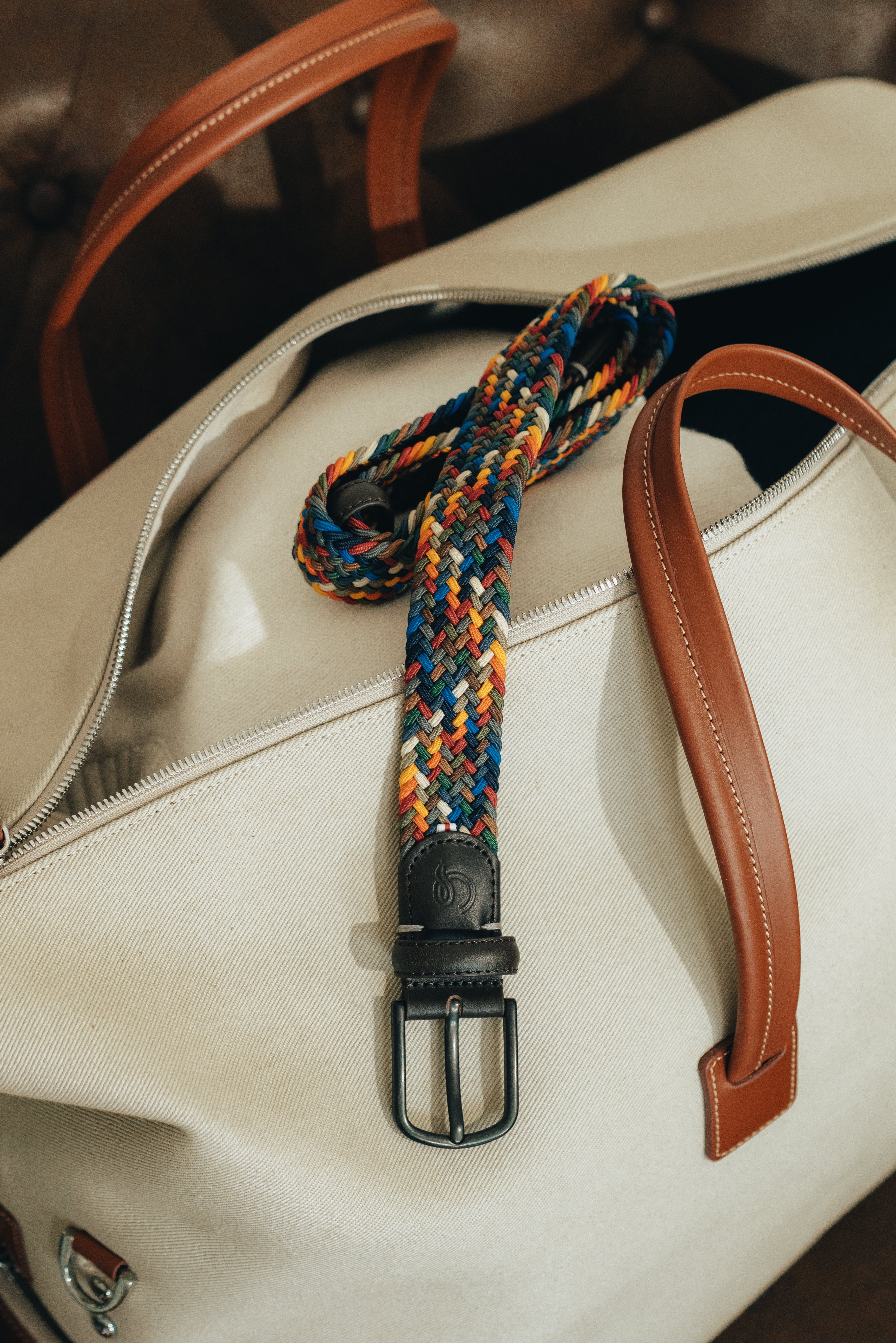 Colorful braided belt with a black buckle on a white bag.