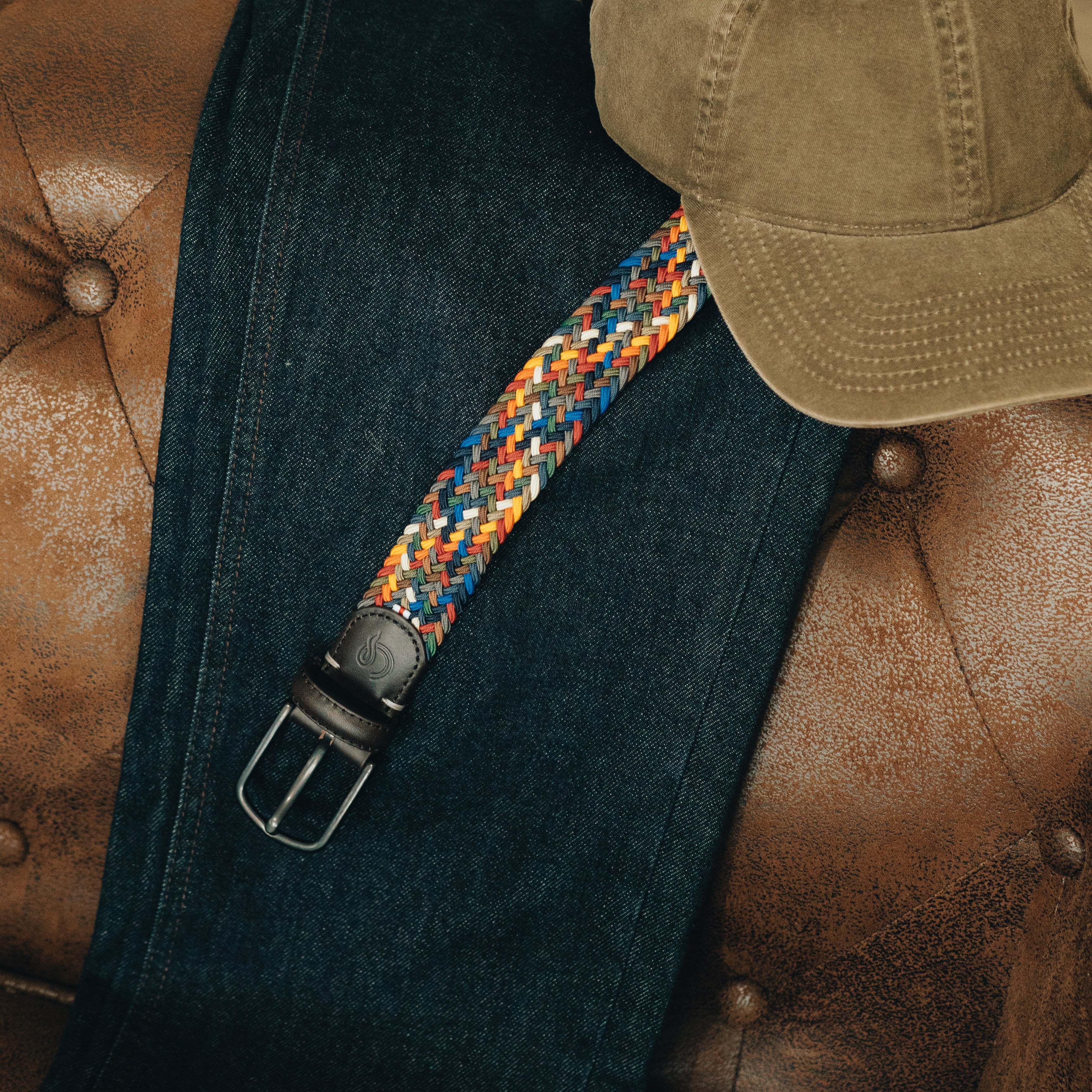 Blue jeans with a colorful strap and brown cap on a brown leather surface