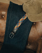 Blue jeans with a colorful strap and brown cap on a brown leather surface