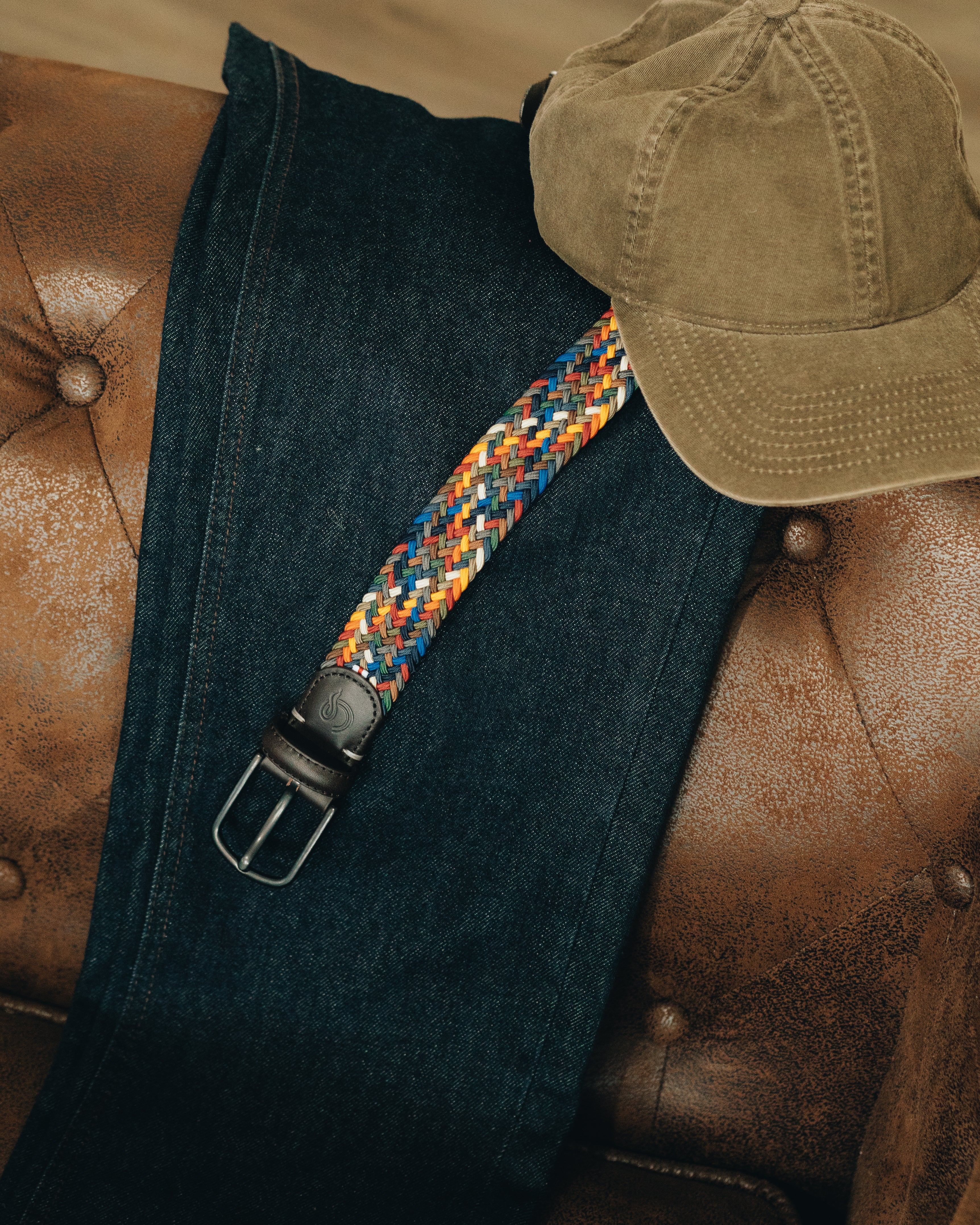Blue jeans with a colorful strap and brown cap on a brown leather surface